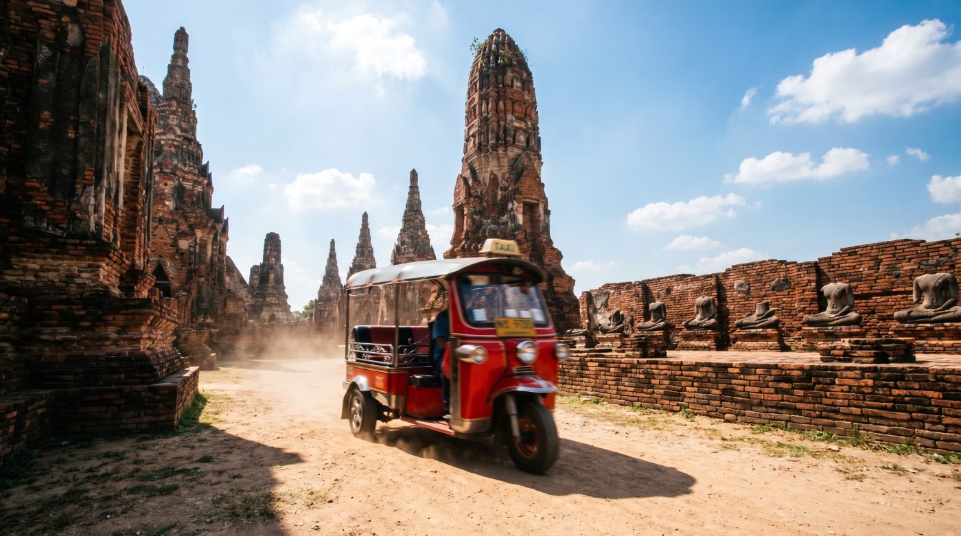 A red tuk-tuk driving past ancient brick ruins at Ayutthaya Historical Park