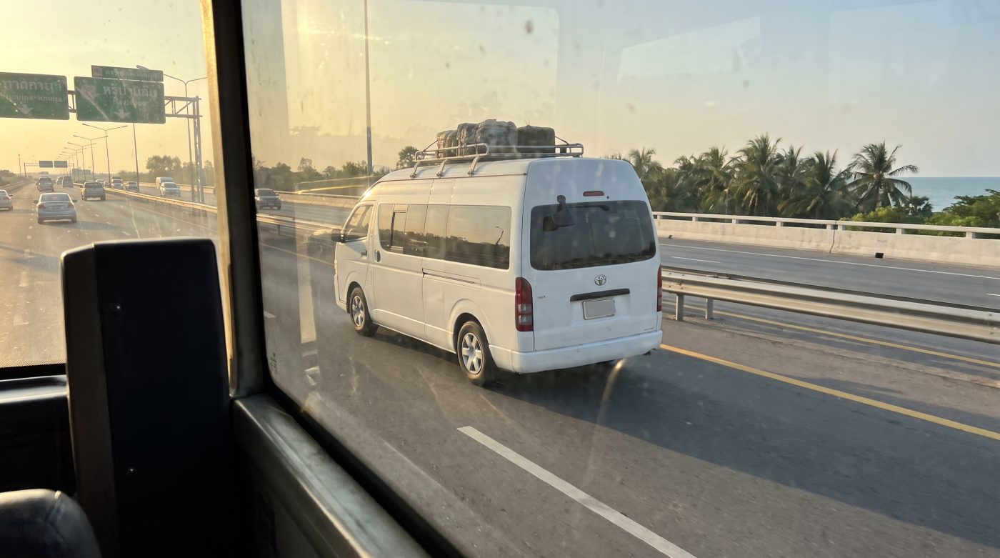 A white passenger minivan driving on a Thai expressway toward Pattaya
