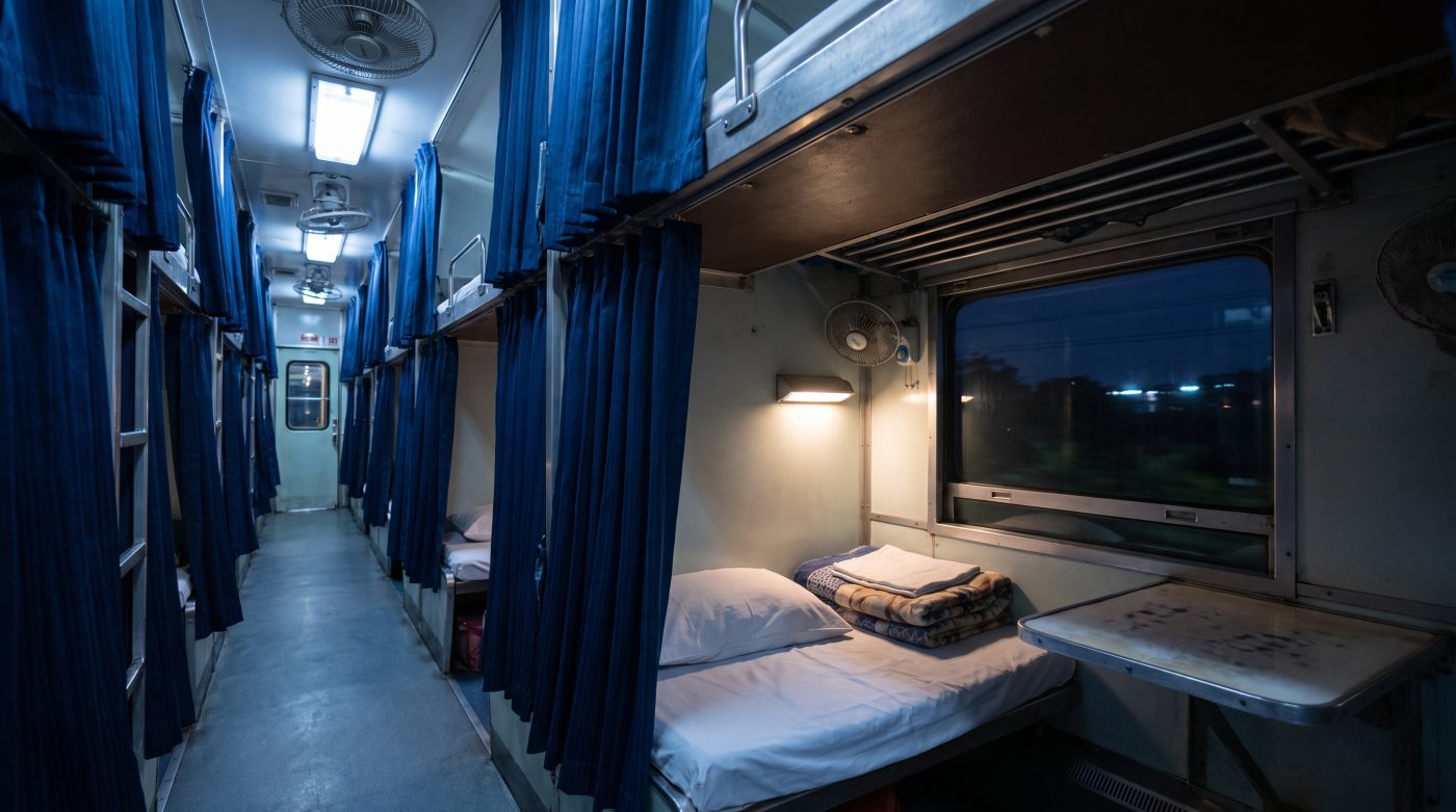 Interior of a Thai second-class overnight sleeper train car with curtained bunk berths at night