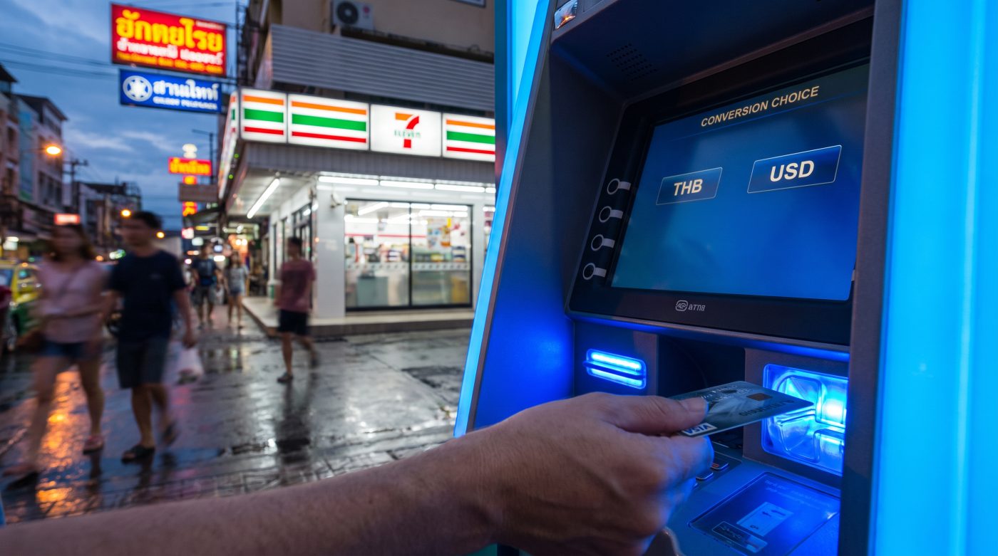 Tourist inserting a card into a Thai ATM with a currency conversion prompt glowing on the screen