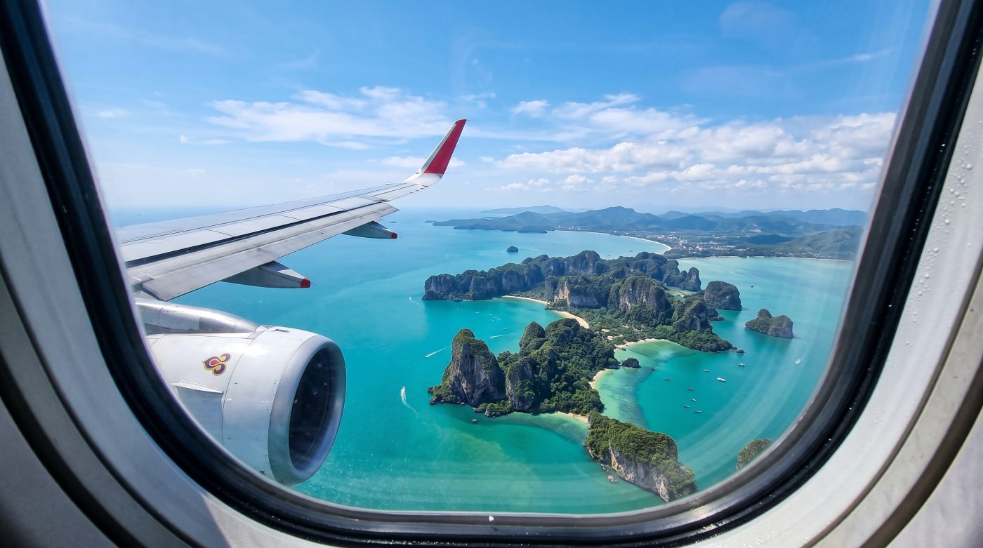 View from an airplane window over turquoise water and green islands off the coast of Thailand